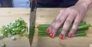 Person chopping green onions on a wooden cutting board with a knife.